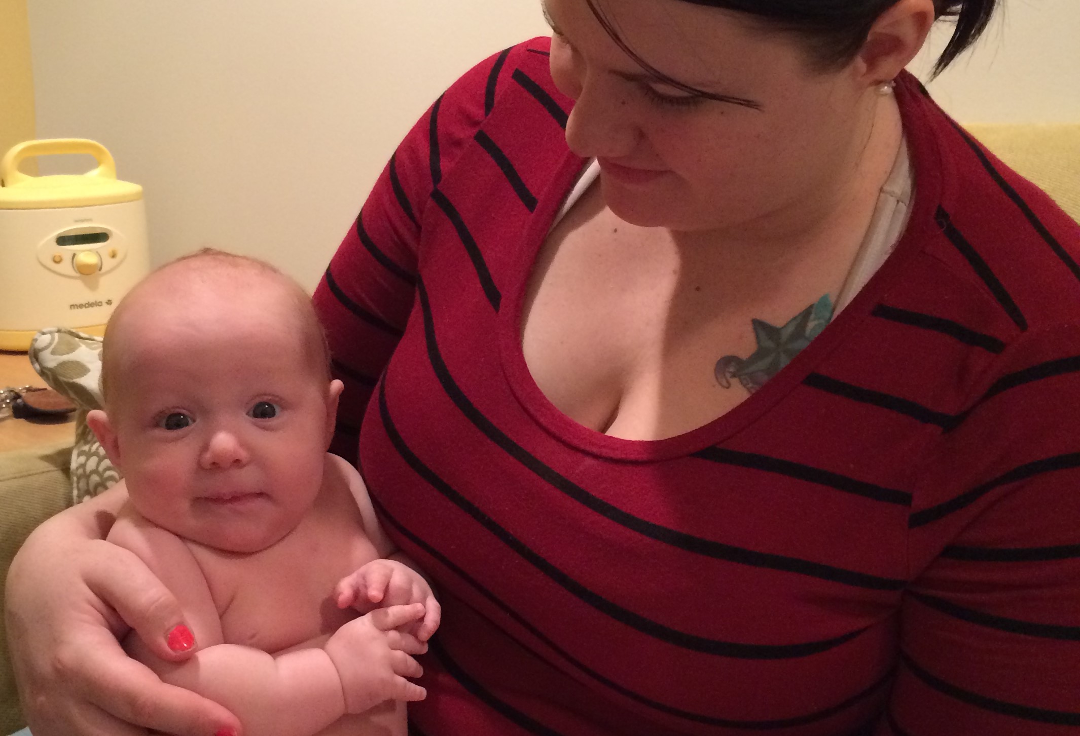 Brunette woman in red striped shirt holding a chubby baby wearing a diaper. She is looking at her baby and the baby is looking at the camera.