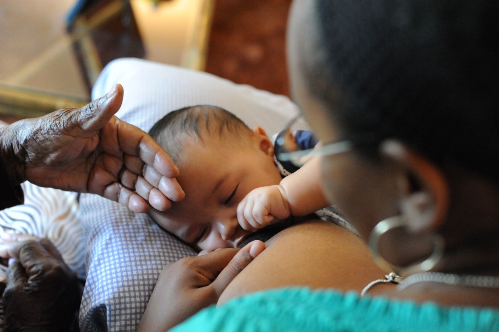 Black woman breastfeeding her infant, while older Black woman's hand rests on infant's forehead